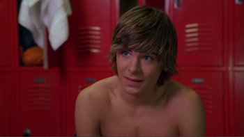 Movie still from “High School Musical” (2006), directed by Kenny Ortega – A young man with brown hair sitting in a room with red lockers; Medium shot, Over the shoulder angle