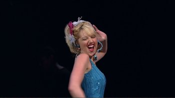 Movie still from “High School Musical” (2006), directed by Kenny Ortega – A woman in a blue dress is laughing and holding her hand up to the side of her head; Medium shot, Low angle