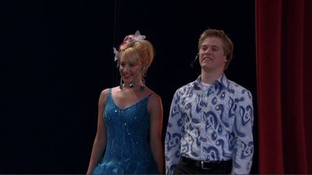 Movie still from “High School Musical” (2006), directed by Kenny Ortega – A man and a woman standing next to each other on a stage; Medium shot, Low angle