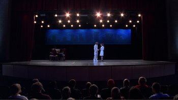 Movie still from “High School Musical” (2006), directed by Kenny Ortega – A couple of people on a stage in front of an audience; Extreme Wide shot, High angle