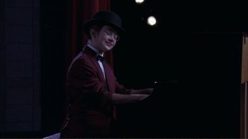 Movie still from “High School Musical” (2006), directed by Kenny Ortega – A man wearing a suit and a top hat; Medium shot, High angle