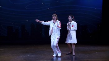 Movie still from “High School Musical” (2006), directed by Kenny Ortega – A man and a woman singing on a stage; Wide shot, Low angle