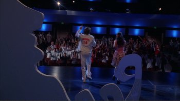 Movie still from “High School Musical” (2006), directed by Kenny Ortega – A couple of people on a stage with a crowd of people in the background; Extreme Wide shot, Low angle