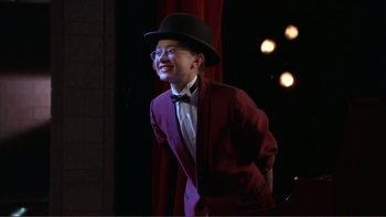 Movie still from “High School Musical” (2006), directed by Kenny Ortega – A young man wearing a suit and a top hat; Medium shot, High angle