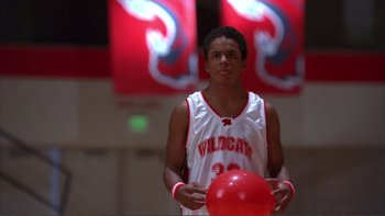 Movie still from “High School Musical” (2006), directed by Kenny Ortega – A young man holding a red ball in a gym; Medium shot, Low angle