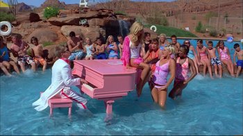 Movie still from “High School Musical 2” (2007), directed by Kenny Ortega – A group of people sitting around a pink piano in a pool; Extreme Wide shot, High angle