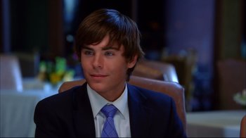 Movie still from “High School Musical 2” (2007), directed by Kenny Ortega – A man in a suit and tie sitting in a chair; Close Up shot, Over the shoulder angle