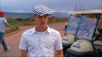 Movie still from “High School Musical 2” (2007), directed by Kenny Ortega – A young man wearing a striped hat standing in front of a golf cart; Close Up shot, Low angle