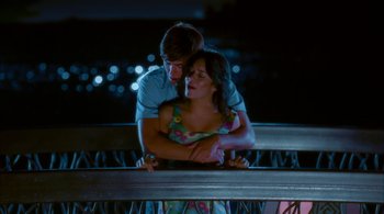 Movie still from “High School Musical 2” (2007), directed by Kenny Ortega – A man and a woman hugging on top of a railing at night; Medium shot, Over the shoulder angle