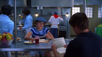 Movie still from “High School Musical 2” (2007), directed by Kenny Ortega – A woman sitting at a table in front of a menu; Medium shot, Over the shoulder angle