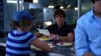 Movie still from “High School Musical 2” (2007), directed by Kenny Ortega – A man sitting at a table in front of a plate of food; Medium shot, Over the shoulder angle