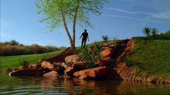 Movie still from “High School Musical 2” (2007), directed by Kenny Ortega – A man standing on a rock wall next to a tree; Extreme Wide shot, Low angle
