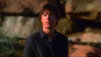 Movie still from “High School Musical 2” (2007), directed by Kenny Ortega – A young man in a black shirt is standing in front of a rock wall; Close Up shot, Over the shoulder angle