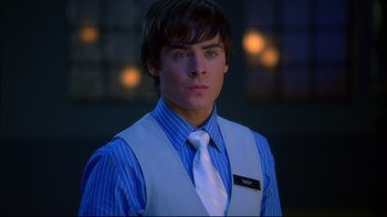 Movie still from “High School Musical 2” (2007), directed by Kenny Ortega – A man in a vest and a tie is standing in front of a building; Close Up shot, Over the shoulder angle