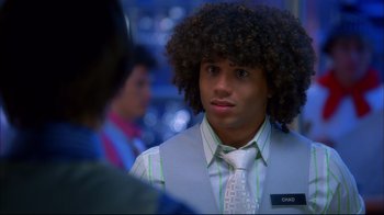 Movie still from “High School Musical 2” (2007), directed by Kenny Ortega – A young man with curly black hair wearing a vest and tie; Close Up shot, Over the shoulder angle
