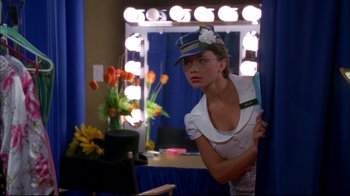 Movie still from “High School Musical 2” (2007), directed by Kenny Ortega – A woman in a hat and glasses in front of a mirror; Medium shot, Low angle