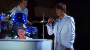 Movie still from “High School Musical 2” (2007), directed by Kenny Ortega – A man in a white jacket is singing; Medium shot, Low angle