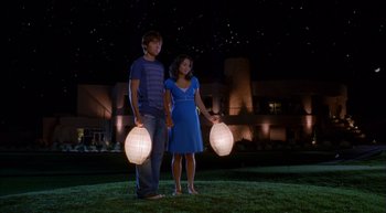 Movie still from “High School Musical 2” (2007), directed by Kenny Ortega – A man and a woman standing in the grass holding paper lanterns; Wide shot, Low angle