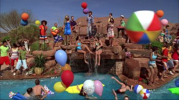 Movie still from “High School Musical 2” (2007), directed by Kenny Ortega – A group of people standing next to a pool with balloons; Extreme Wide shot, High angle