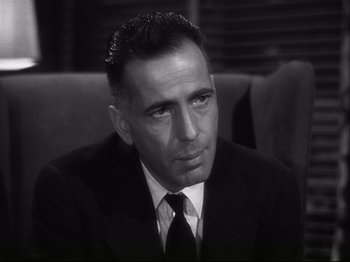 Movie still from “High Sierra” (1940), directed by Raoul Walsh – A man wearing a suit and tie sitting on a couch; Close Up shot, Over the shoulder angle