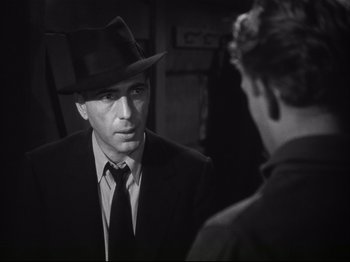 Movie still from “High Sierra” (1940), directed by Raoul Walsh – A black and white photo of a man wearing a suit and hat; Close Up shot, Over the shoulder angle
