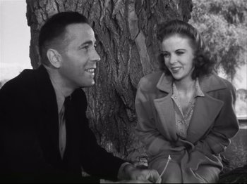 Movie still from “High Sierra” (1940), directed by Raoul Walsh – A man and a woman sitting next to a tree; Medium shot, Low angle