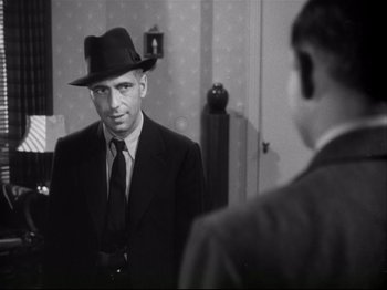 Movie still from “High Sierra” (1940), directed by Raoul Walsh – A black and white photo of a man in a suit and hat; Close Up shot, Over the shoulder angle