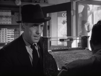 Movie still from “High Sierra” (1940), directed by Raoul Walsh – A black and white photo of a man wearing a suit and a hat; Medium shot, Over the shoulder angle