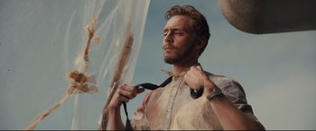 Movie still from “High-Rise” (2015), directed by Ben Wheatley – A man with a tie is holding his tie up; Medium shot, Low angle