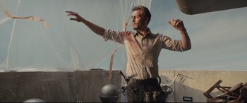 Movie still from “High-Rise” (2015), directed by Ben Wheatley – A man standing on top of a building with his arms outstreched; Medium shot, Low angle