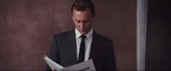 Movie still from “High-Rise” (2015), directed by Ben Wheatley – A man in a suit and tie holding a book; Medium shot, Low angle