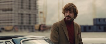 Movie still from “High-Rise” (2015), directed by Ben Wheatley – A man in a brown jacket and a red sweater; Medium shot, Low angle