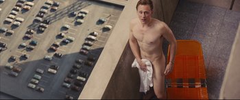 Movie still from “High-Rise” (2015), directed by Ben Wheatley – A man with no shirt is standing on a balcony with a towel; Wide shot, High angle