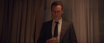 Movie still from “High-Rise” (2015), directed by Ben Wheatley – A man in a suit and tie holding a glass; Medium shot, Over the shoulder angle