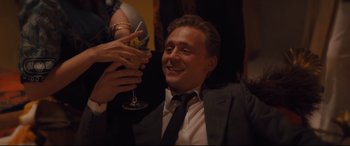 Movie still from “High-Rise” (2015), directed by Ben Wheatley – A man sitting in front of a woman holding up a wine glass; Medium shot, High angle