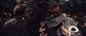 Movie still from “High-Rise” (2015), directed by Ben Wheatley – A man is standing in front of a mirror; Medium shot, Over the shoulder angle