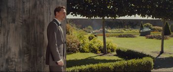 Movie still from “High-Rise” (2015), directed by Ben Wheatley – A man in a suit and tie standing next to a tree; Wide shot, Over the shoulder angle