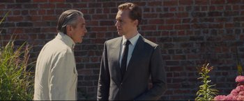 Movie still from “High-Rise” (2015), directed by Ben Wheatley – A man in a suit and tie standing next to another man in a suit and tie; Medium shot, Over the shoulder angle
