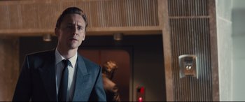 Movie still from “High-Rise” (2015), directed by Ben Wheatley – A person wearing a suit and tie; Medium shot, Low angle
