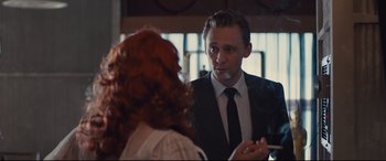 Movie still from “High-Rise” (2015), directed by Ben Wheatley – A man in a suit and tie talking to a woman in front of a mirror; Medium shot, Over the shoulder angle