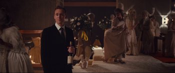 Movie still from “High-Rise” (2015), directed by Ben Wheatley – A man holding a bottle of wine in front of two women; Wide shot, Over the shoulder angle