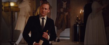 Movie still from “High-Rise” (2015), directed by Ben Wheatley – A man in a black suit holding a bottle of wine; Medium shot, Over the shoulder angle