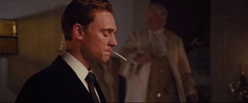 Movie still from “High-Rise” (2015), directed by Ben Wheatley – A person with a cigarette in his mouth; Medium shot, Over the shoulder angle