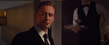 Movie still from “High-Rise” (2015), directed by Ben Wheatley – A person wearing a suit and tie; Medium shot, Over the shoulder angle
