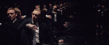 Movie still from “High-Rise” (2015), directed by Ben Wheatley – A man in a black suit and white shirt is reflected in a mirror; Medium shot, High angle