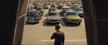Movie still from “High-Rise” (2015), directed by Ben Wheatley – A man in a suit standing in a parking lot; Wide shot, High angle