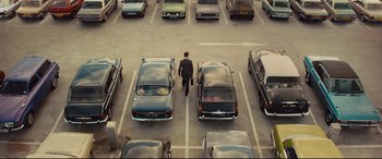 Movie still from “High-Rise” (2015), directed by Ben Wheatley – A man in a parking lot with many parked cars; Extreme Wide shot, High angle