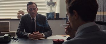 Movie still from “High-Rise” (2015), directed by Ben Wheatley – Two people sitting at a table with a cigarette in their mouth; Medium shot, Over the shoulder angle