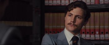 Movie still from “High-Rise” (2015), directed by Ben Wheatley – A man in a suit and tie with a mustache; Close Up shot, Over the shoulder angle