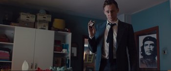 Movie still from “High-Rise” (2015), directed by Ben Wheatley – A man in a suit and tie holding a small object; Medium shot, Low angle